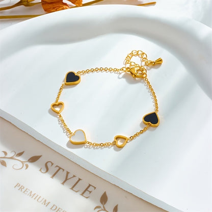 Brazalete Alma Cruz de acero inoxidable dorado con corazones de esmalte negro y blanco, cadena ajustable.