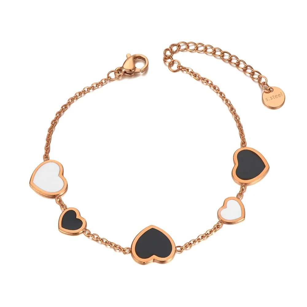 Brazalete Alma Cruz de acero inoxidable en tono oro rosa con dijes de corazón esmaltados en blanco y negro.